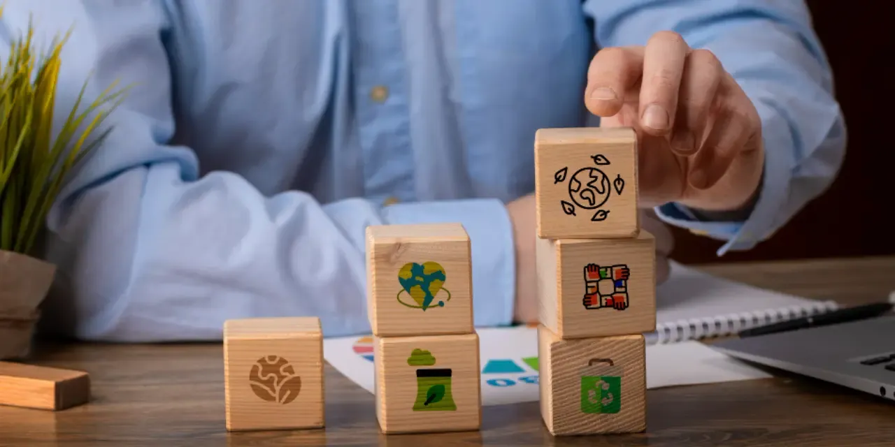 Person stacking wooden blocks with sustainability and environmental responsibility icons.