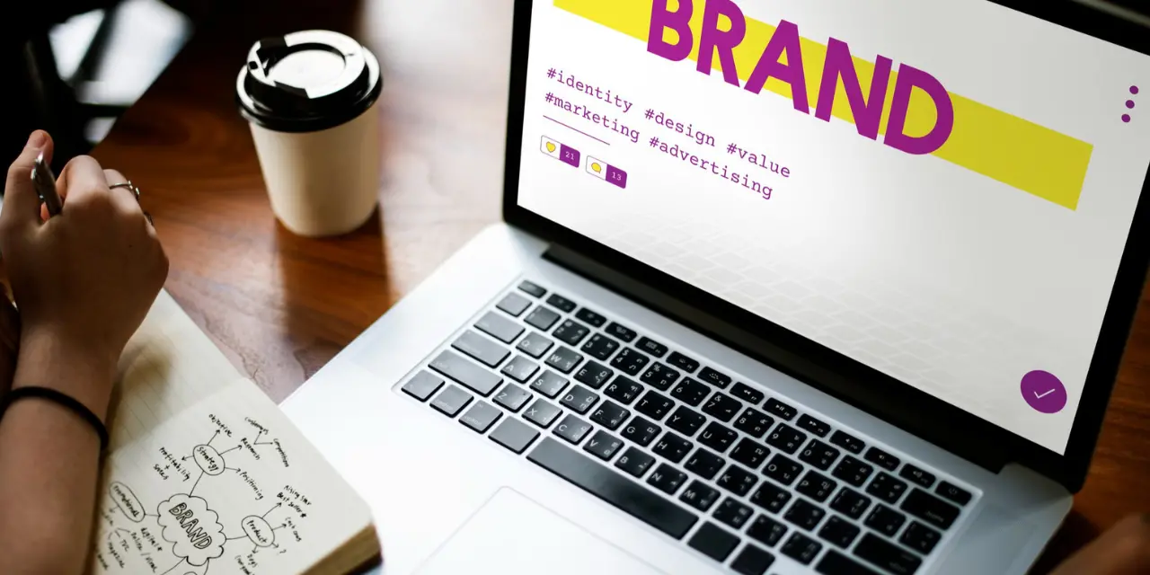 Laptop screen displaying the word "BRAND" and marketing hashtags.
