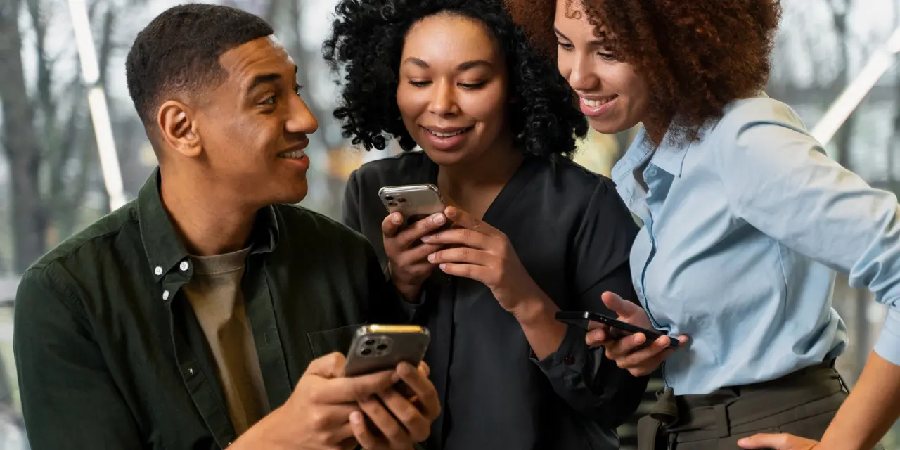Três jovens profissionais sorrindo e fazendo networking usando seus smartphones, compartilhando cartões de visita digitais em um ambiente de escritório moderno.