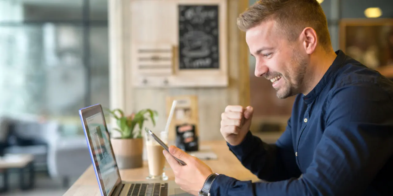 Smiling entrepreneur sharing a digital business card from a smartphone while working on a laptop.